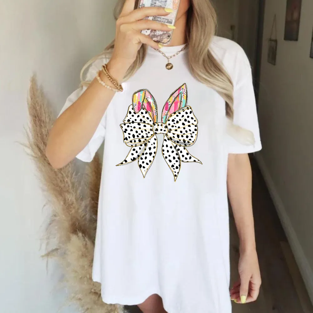 The Bow Is Made Of Black And White Polka Dots, The Bunny Ears Have Colorful Feather-Like Patterns, And The T-Shirt Is Casual.