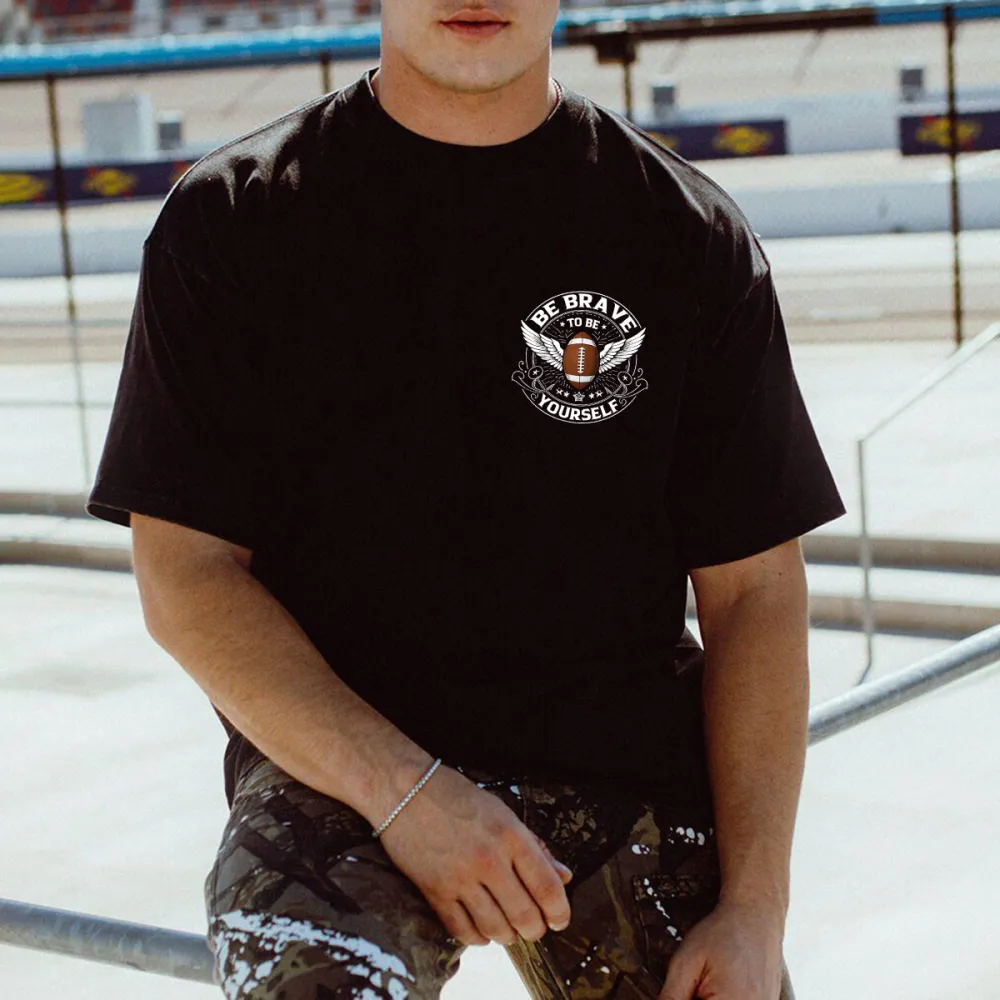 This Is A Graphic T-Shirt With Sports And Inspirational Elements. There Is A Rugby Ball In The Middle And Wings On Both Sides. The Words 