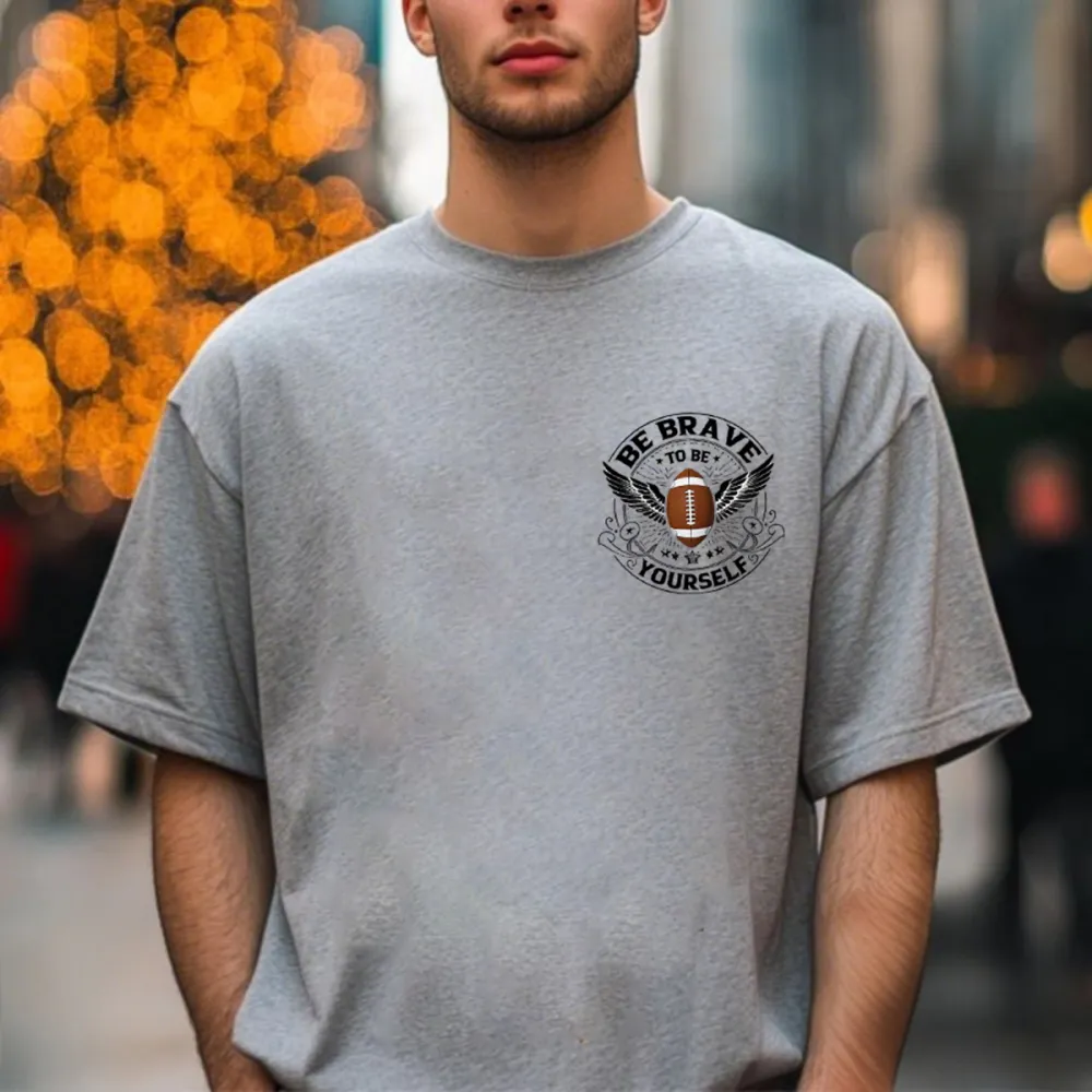 This Is A Graphic T-Shirt With Sports And Inspirational Elements. There Is A Rugby Ball In The Middle And Wings On Both Sides. The Words 