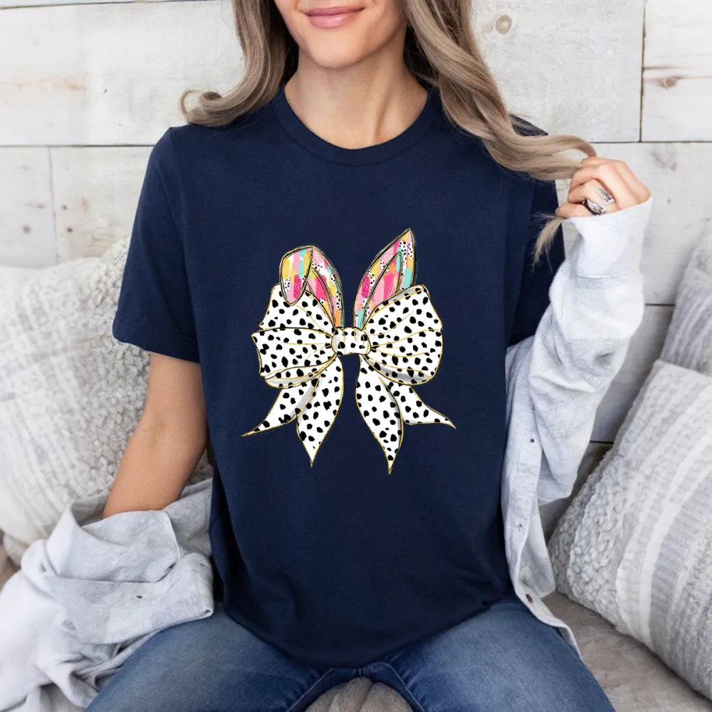 The Bow Is Made Of Black And White Polka Dots, The Bunny Ears Have Colorful Feather-Like Patterns, And The T-Shirt Is Casual.