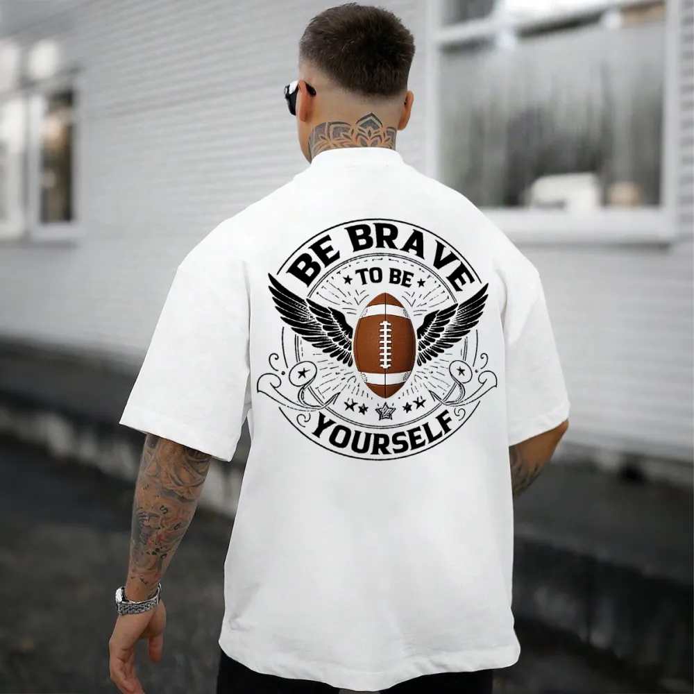 This Is A Graphic T-Shirt With Sports And Inspirational Elements. There Is A Rugby Ball In The Middle And Wings On Both Sides. The Words 