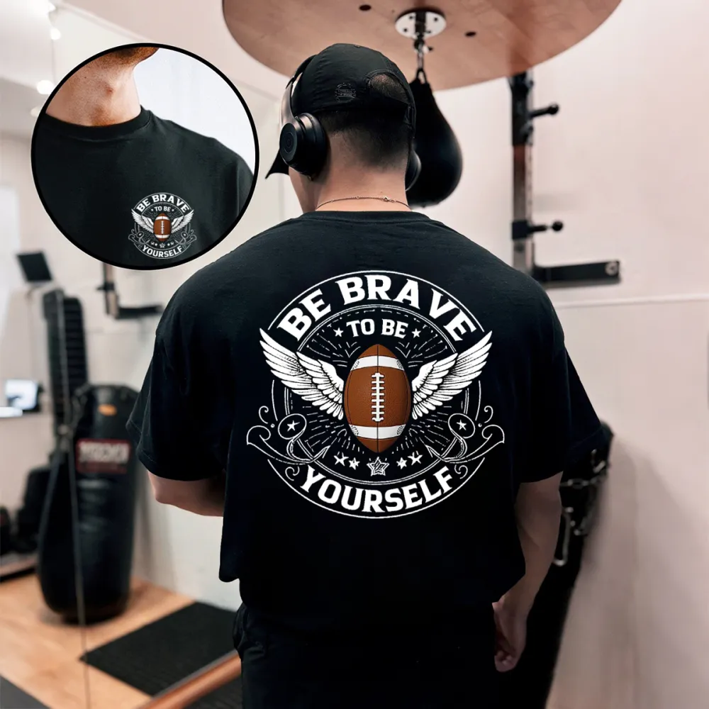 This Is A Graphic T-Shirt With Sports And Inspirational Elements. There Is A Rugby Ball In The Middle And Wings On Both Sides. The Words 